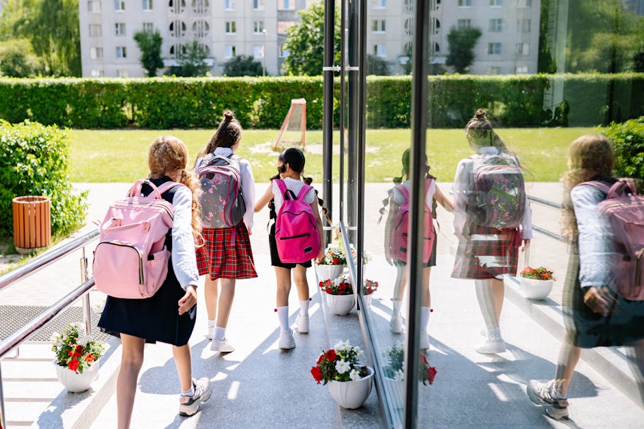 Five girls with backpacks walking into school on a sunny day.